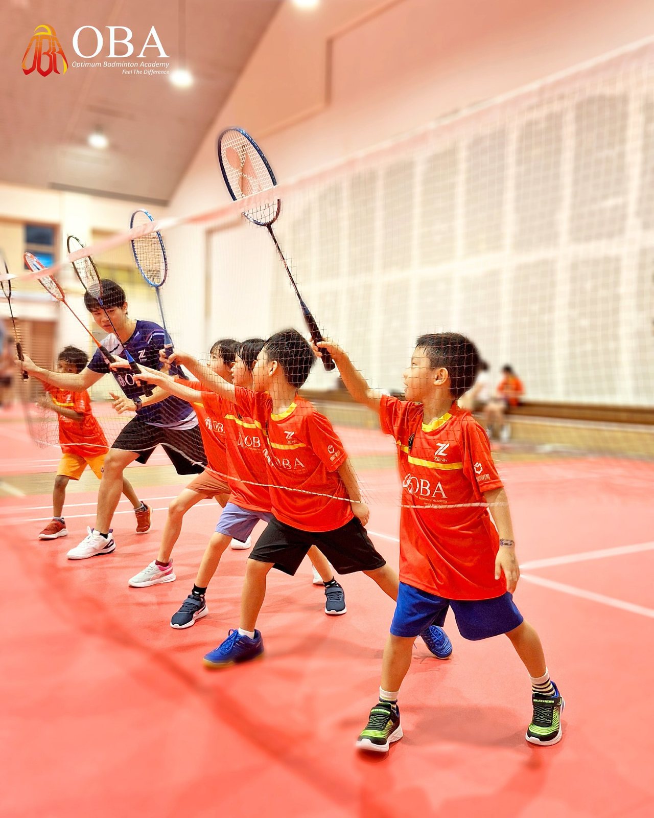 Coach and campers in red OBA jerseys raising their rackets together at the net