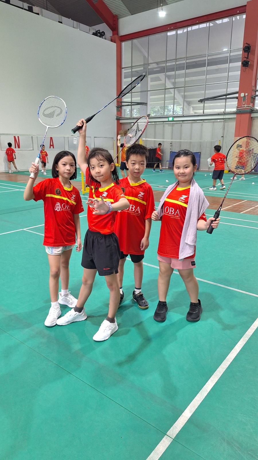 Four children in OBA kit standing together on court with their rackets raised