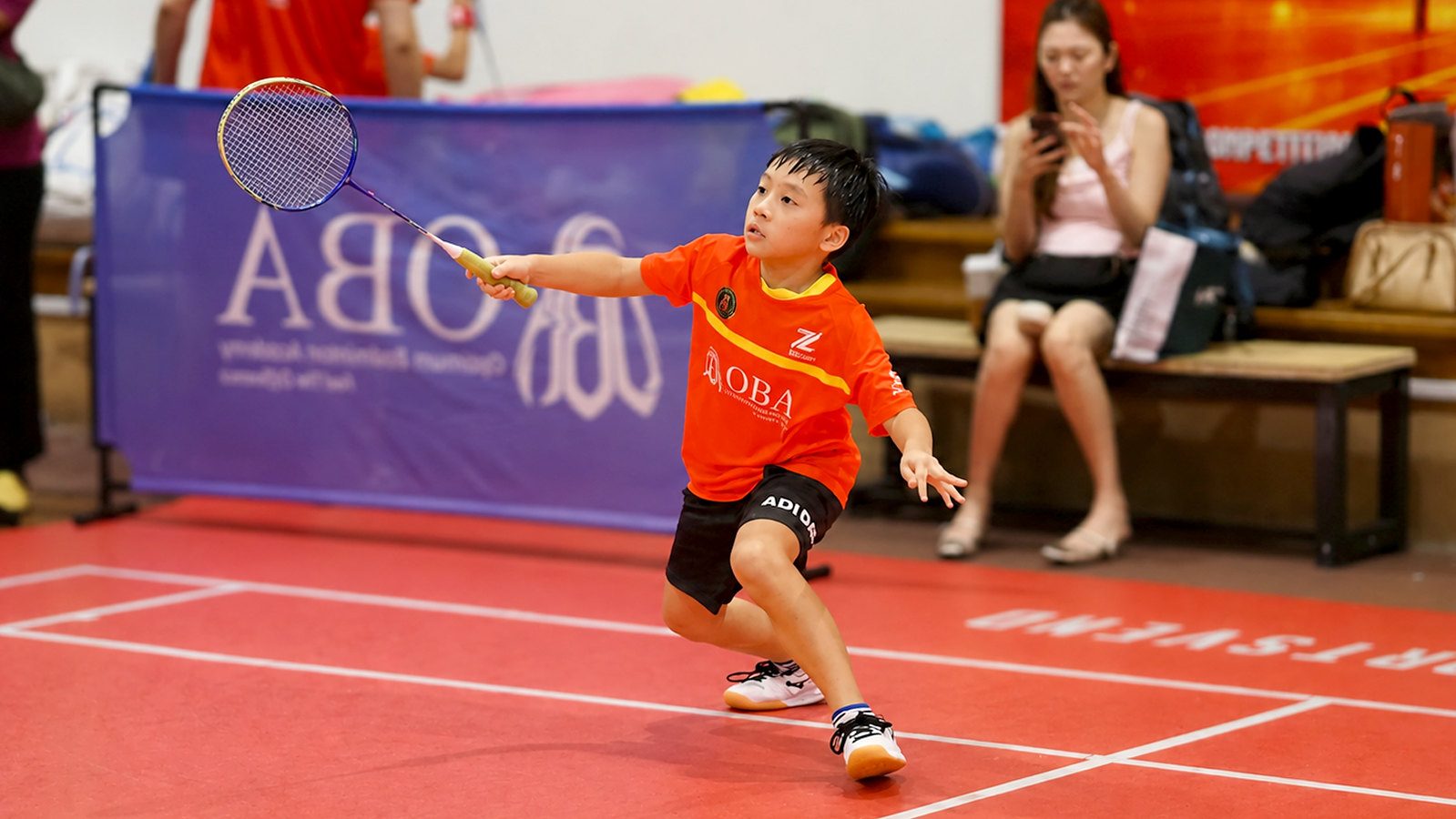 A junior in an orange OBA jersey lunging for a shot