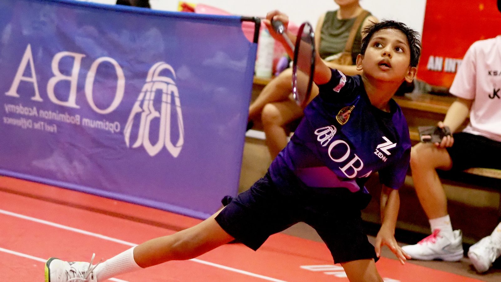 A player in a purple OBA jersey lunging low for a shot