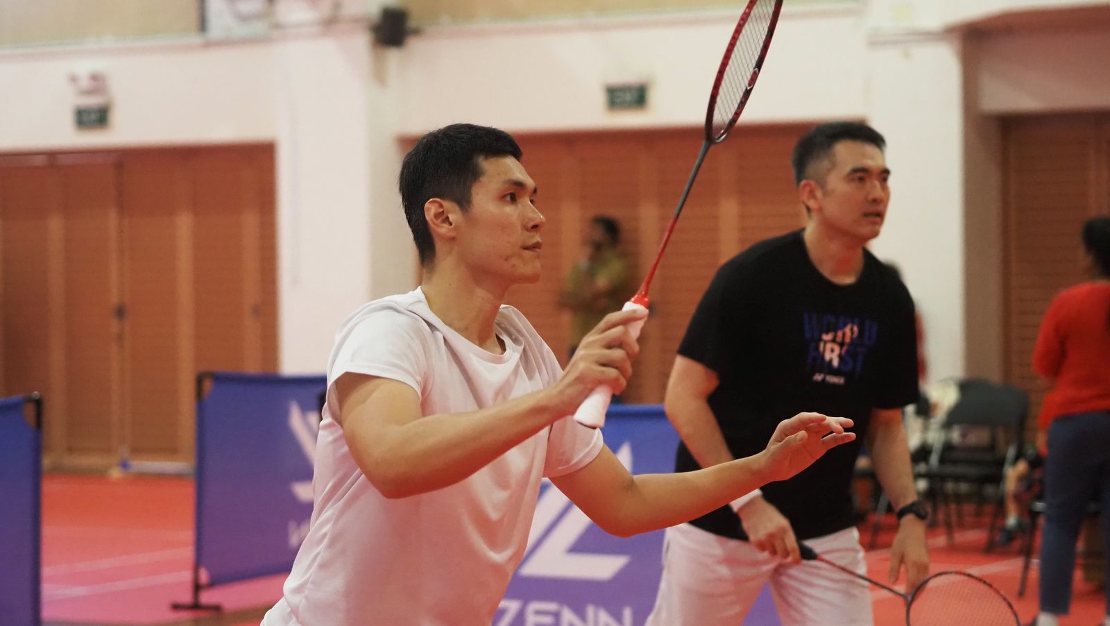 A doubles player reaching for the shuttle at the net
