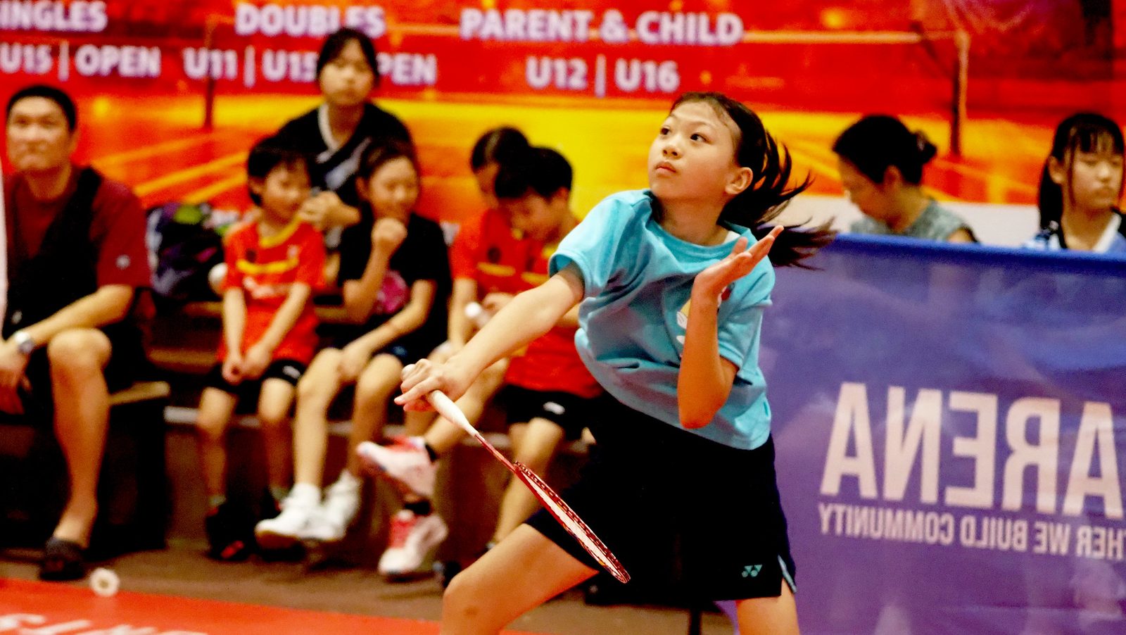 A girl playing a forehand in front of the Parent and Child event banner
